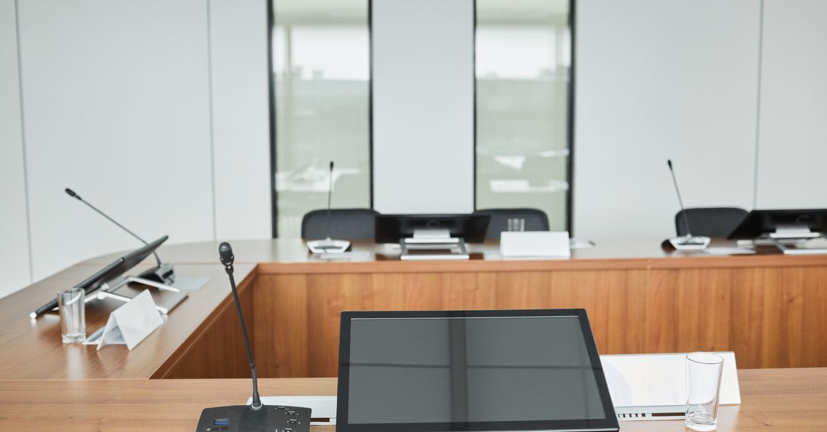 Empty conference room setup with microphones, monitors, and sleek wooden tables ready for meetings.