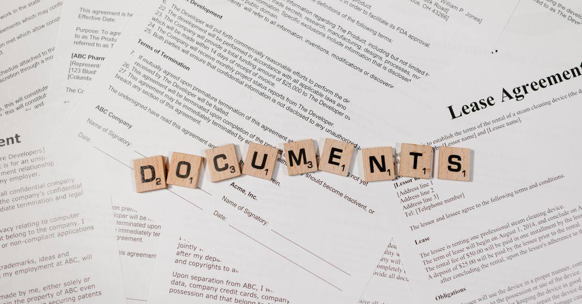 Top view of scrabble tiles spelling 'DOCUMENTS' on various contracts and agreements.