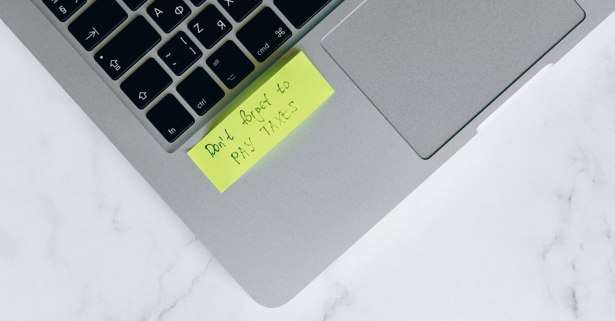 Close-up of a sticky note on a laptop reminding to pay taxes, emphasizing tax season.