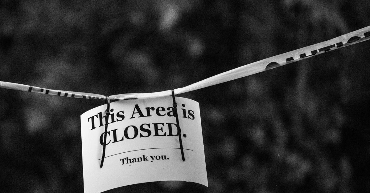 A black and white photo of a sign reading 'This Area is CLOSED.' in a blurred outdoor setting.