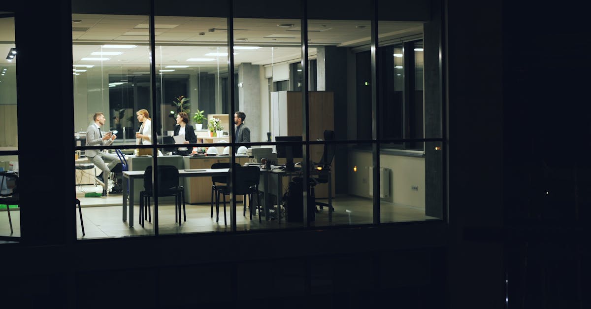 A nighttime office meeting with professionals working in a modern glass-walled office.