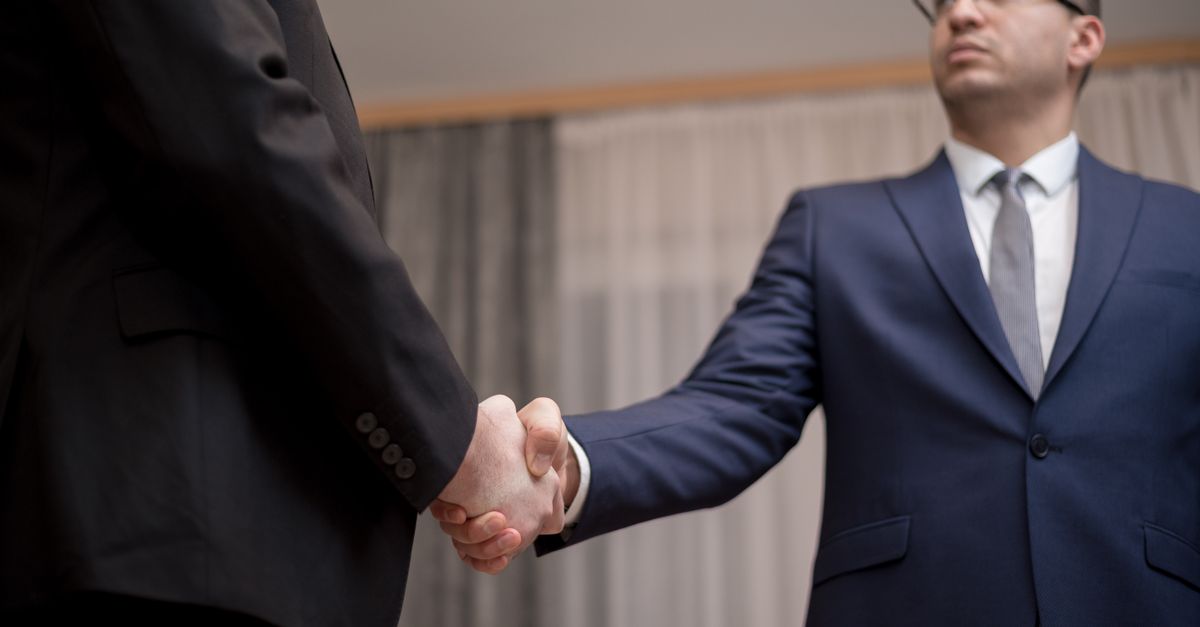Two businessmen in formal attire shaking hands during a meeting.