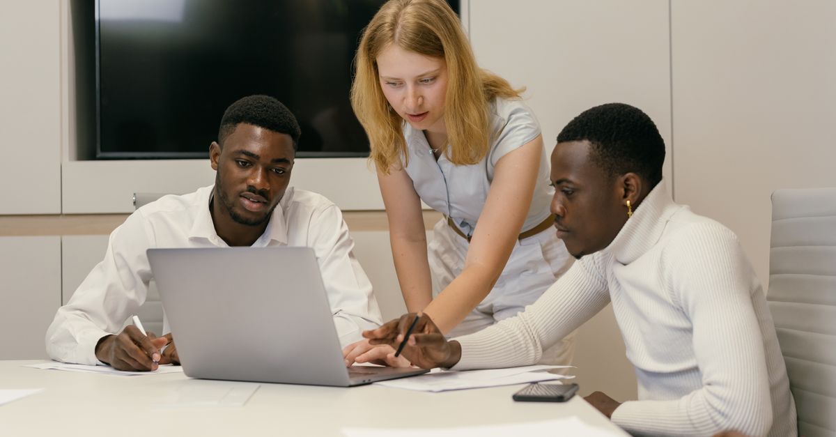 Diverse team working together in a modern office, discussing ideas and collaborating on a laptop.