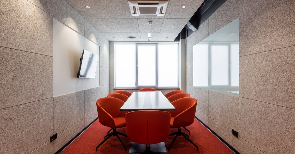 Orange chairs placed around white table in modern conference room with window and TV on wall in contemporary business center