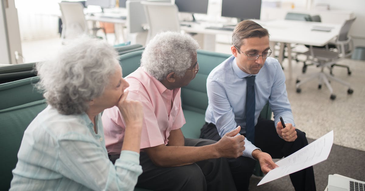 Business professional consults elderly clients in an office setting. Collaborative discussion, paperwork visible.
