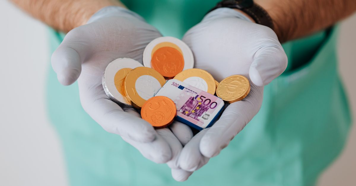 From above crop anonymous medical worker in rubber disposable gloves holding in hands chocolate coins