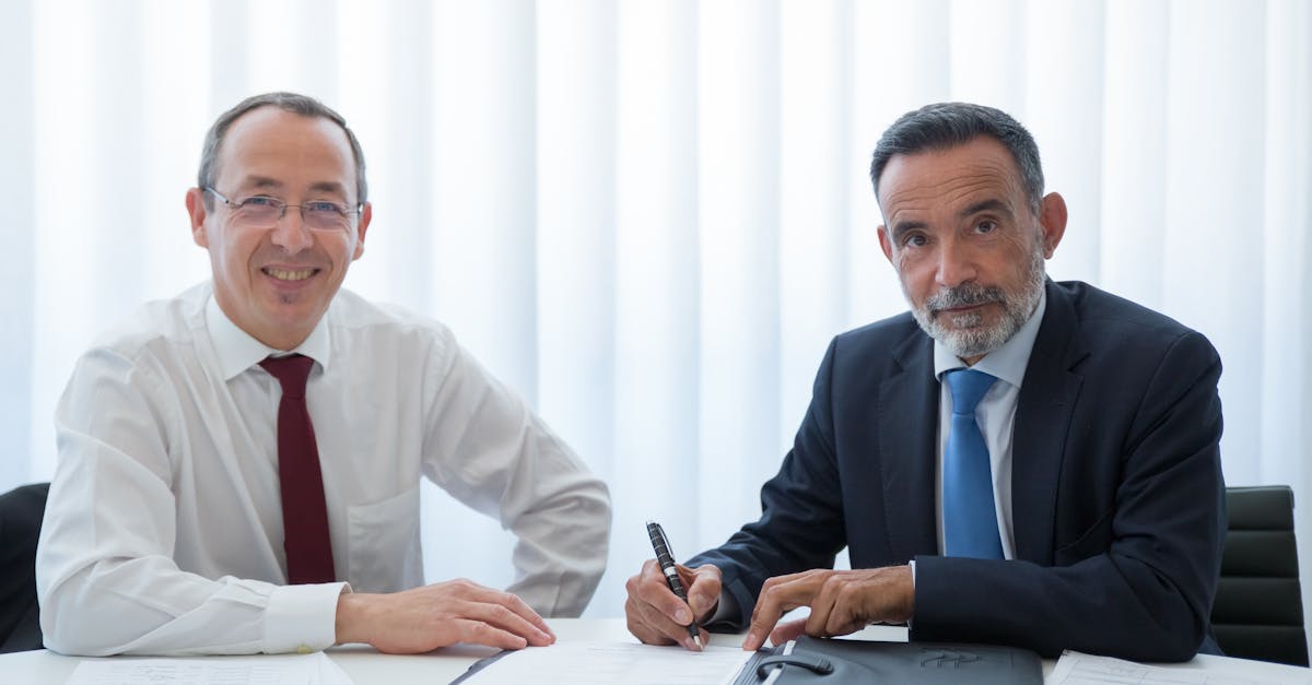 Two businessmen discussing and signing documents at a bright office table.