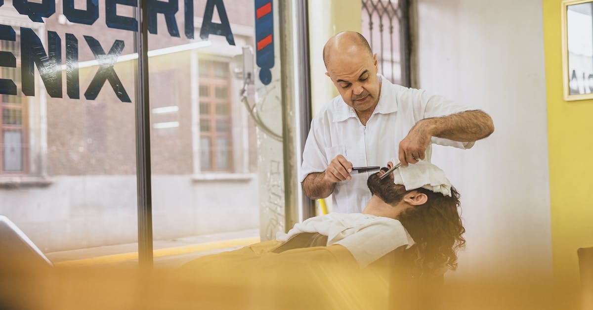 Barber performing a classic straight razor shave on a client in a bright barbershop.
