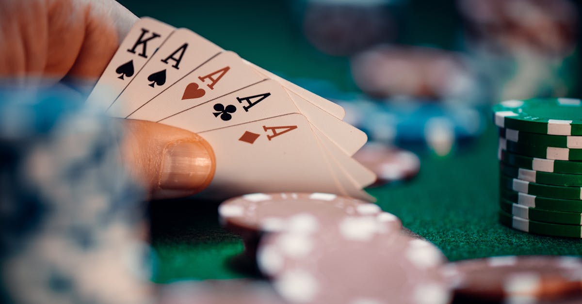 Close-up of poker hand holding four aces and kings with colorful chips on green table for high-stakes gaming.