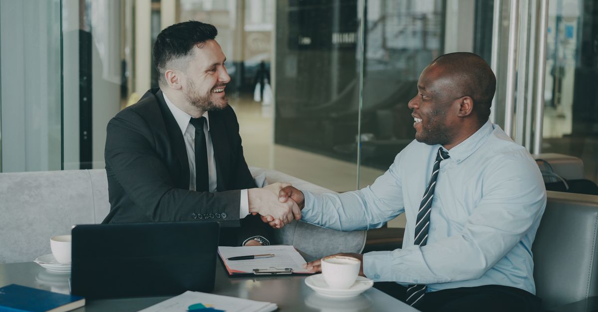 Two businessmen shaking hands over a deal at a modern office.