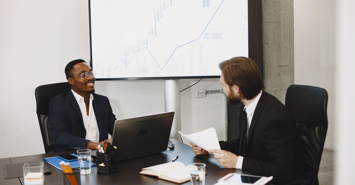 Two businessmen in a professional meeting discussing data on a large screen in a modern office.