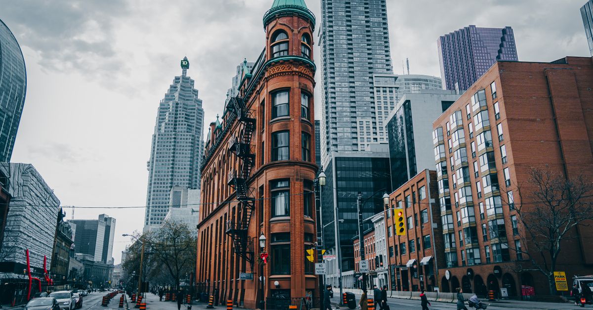 View of the iconic Flatiron Building amidst Toronto's urban skyline on a cloudy day.