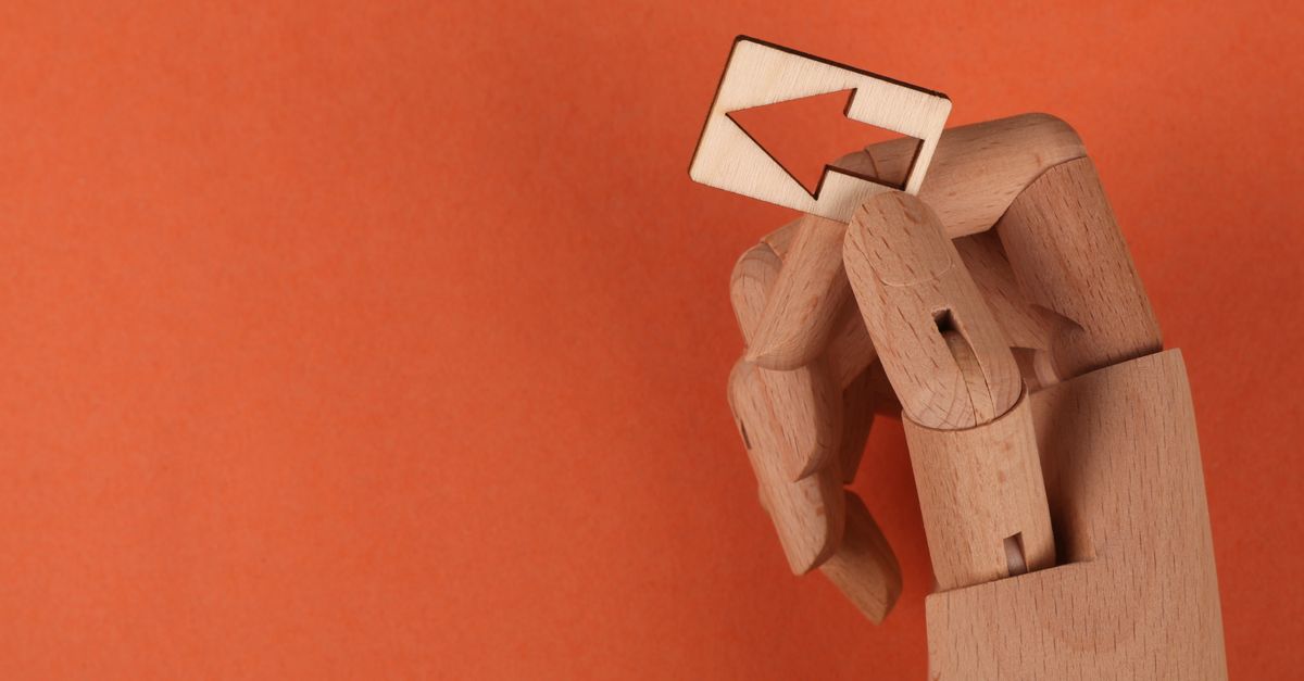 Conceptual image of a wooden mannequin hand holding a wooden arrow against an orange backdrop.