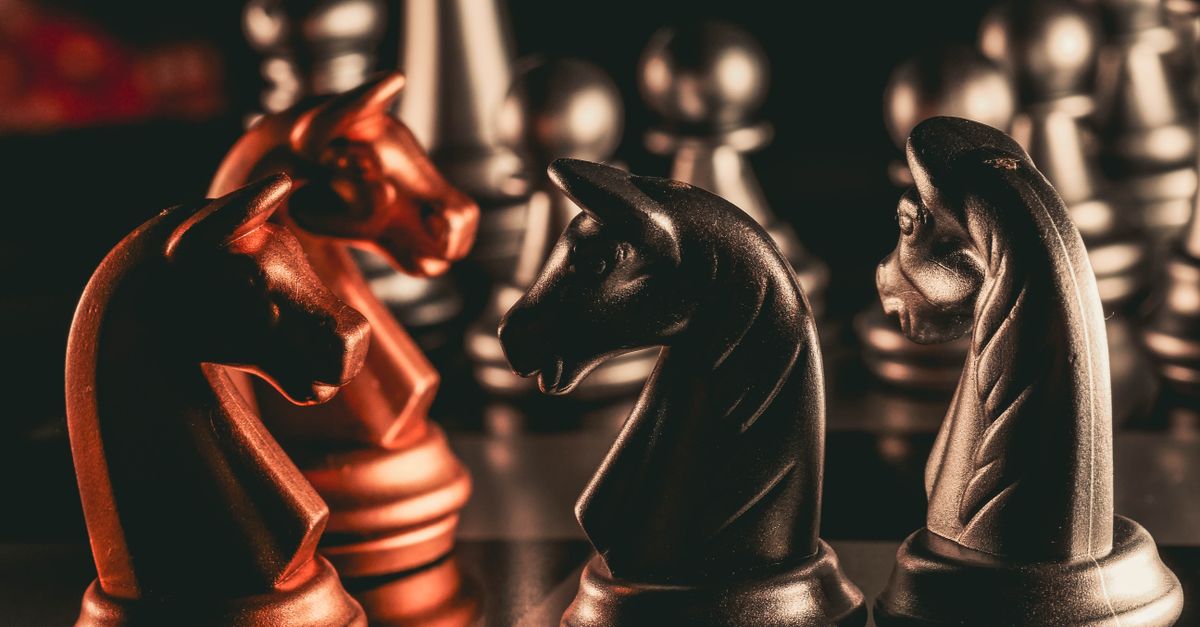 Dramatic close-up of metallic chess knights on a chessboard, showcasing strategic play.
