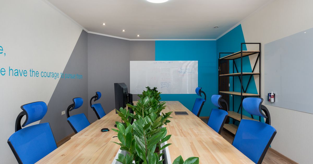 Armchairs at table with green plants placed in light conference room with inscription on wall and shelves in office building