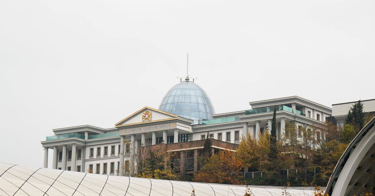 A modern palace with a dome surrounded by autumn trees under an overcast sky.