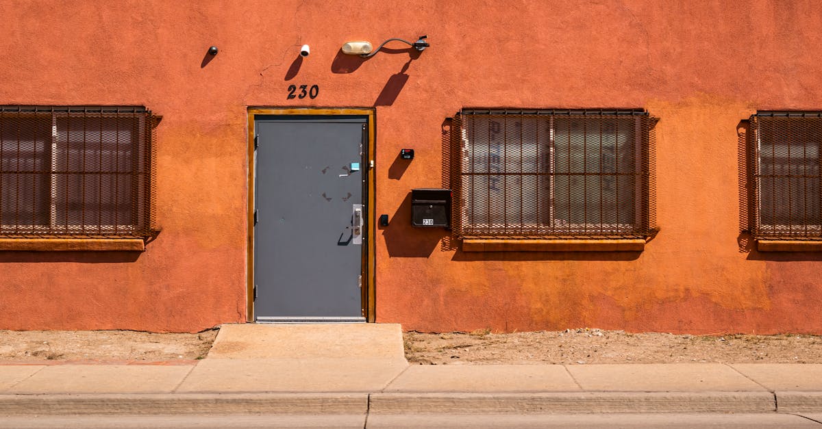 An orange facade with a sturdy metal door and barred windows under bright daylight.