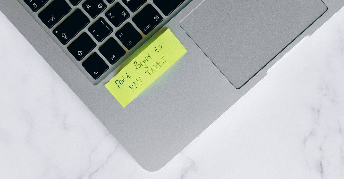 Close-up of a sticky note on a laptop reminding to pay taxes, emphasizing tax season.