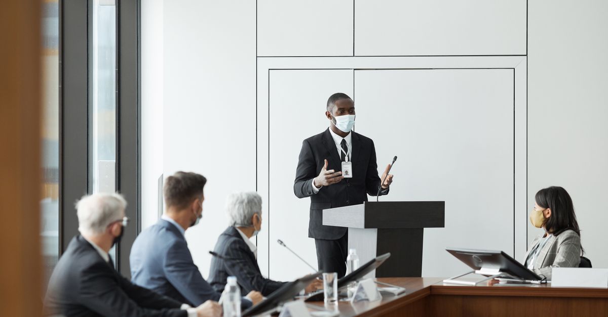Business professionals in masks hold a meeting indoors, highlighting new normal practices during pandemic times.