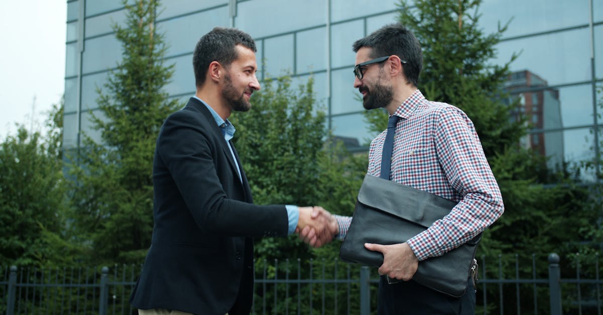 Two businessmen shaking hands outside a modern office building, symbolizing partnership.