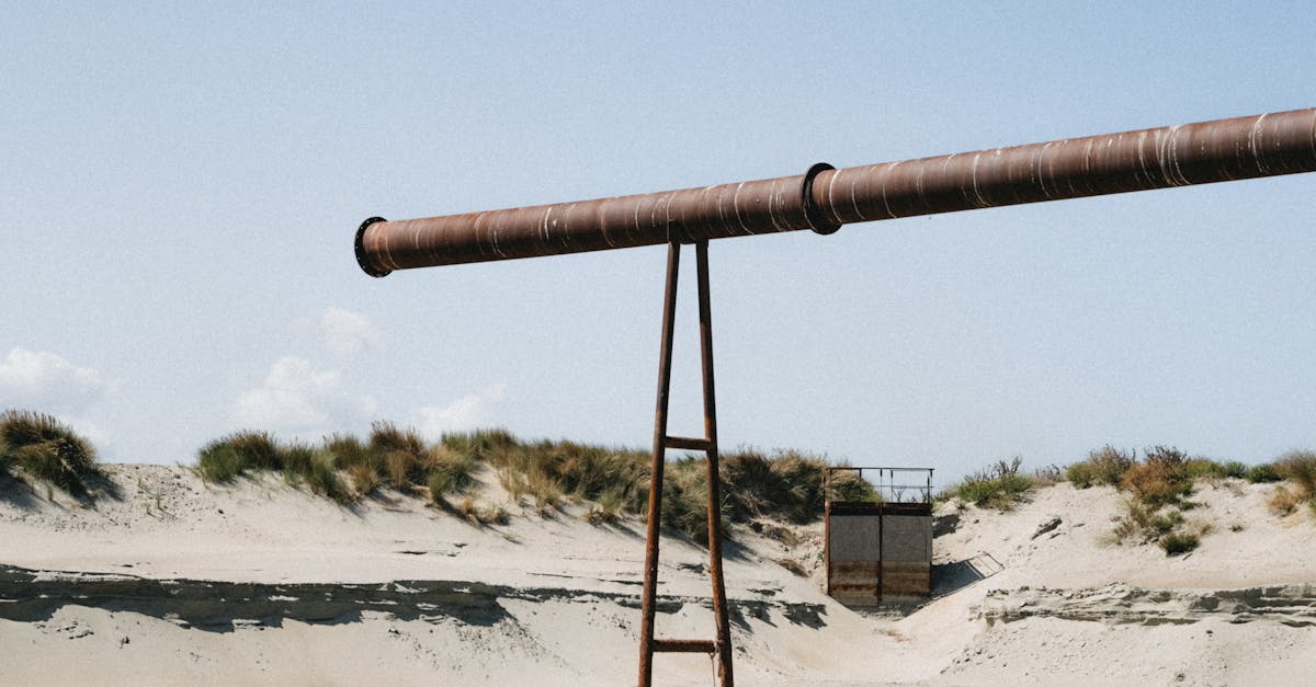 A large rusty pipe stretching across sand dunes in Dunkerque, France, under a clear sky.
