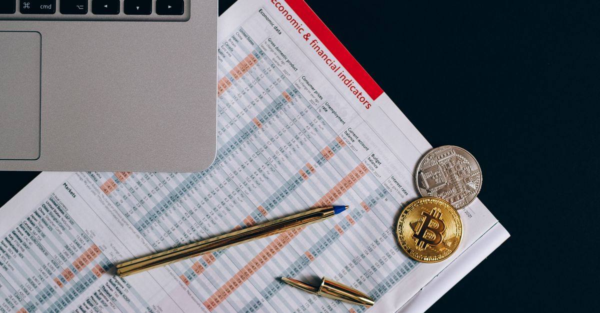 Top view of bitcoin coins on financial documents beside a laptop keyboard.