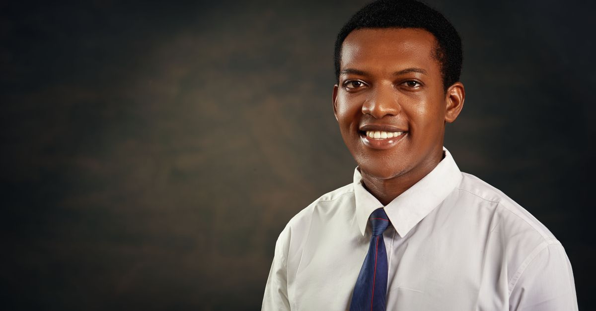 Smiling young adult man in formal attire against dark background, ideal for business or profile use.