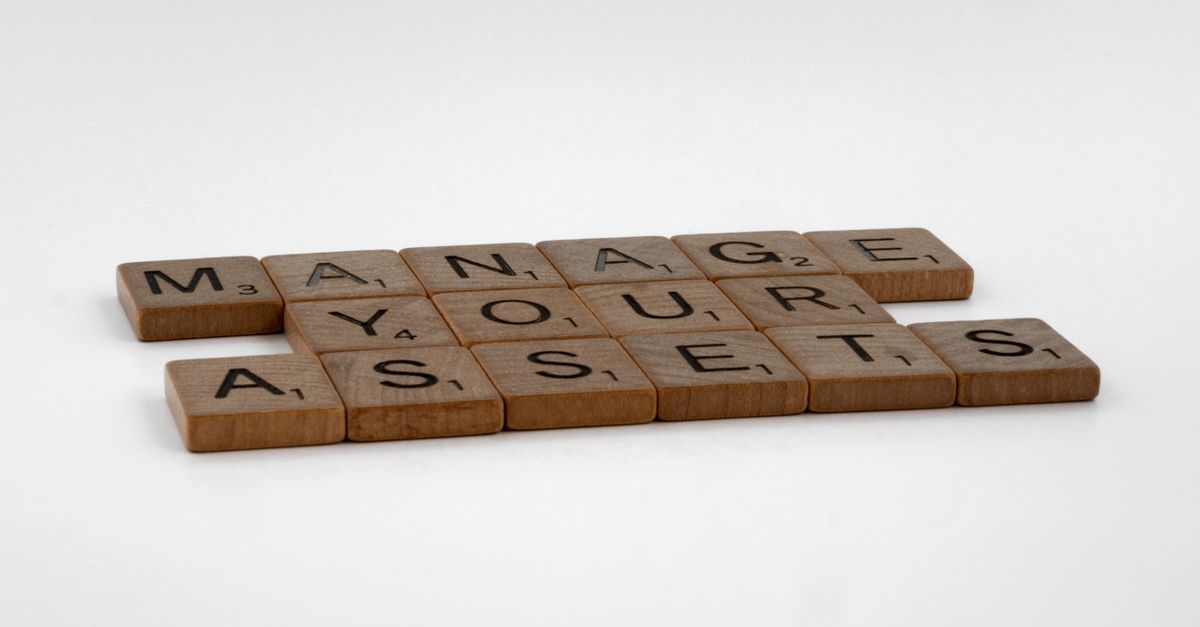 Wooden Scrabble tiles spelling 'Manage Your Assets' on a white background.