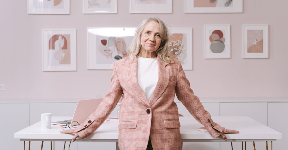 Elderly woman in pink blazer confidently posing in a stylish home office environment.