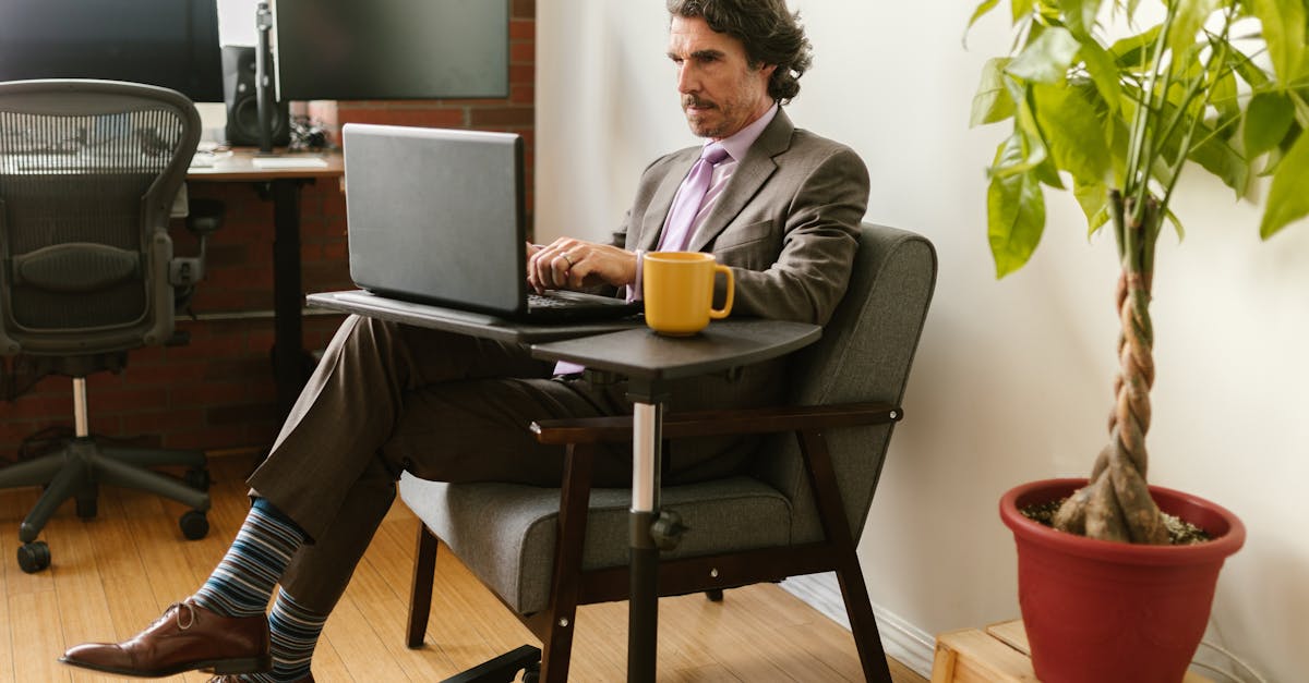 A businessman in formal attire working on a laptop in a modern office environment with an indoor plant.