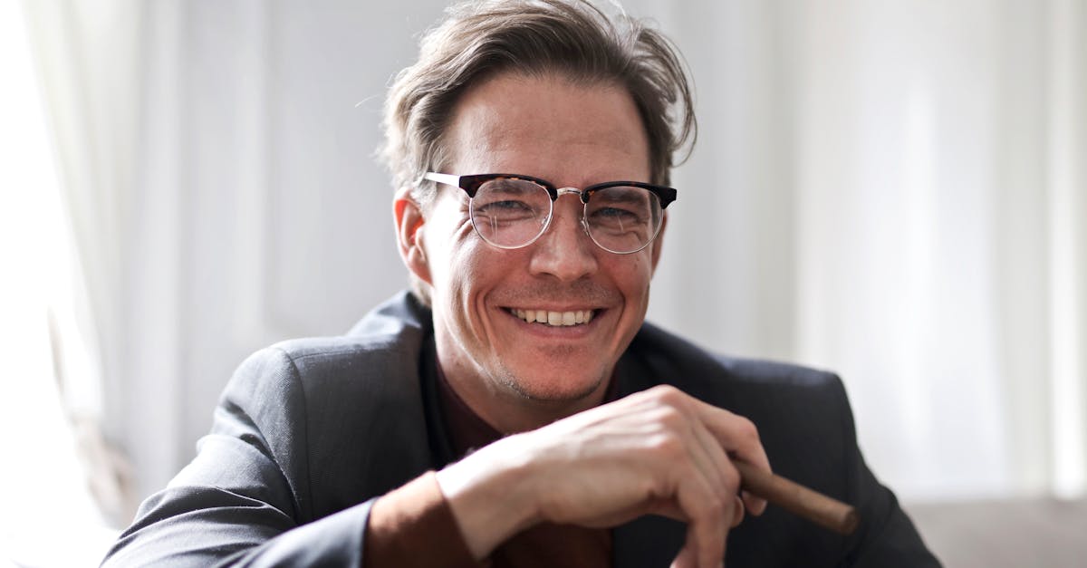 Cheerful businessman in glasses and suit holding a cigar, indoors.