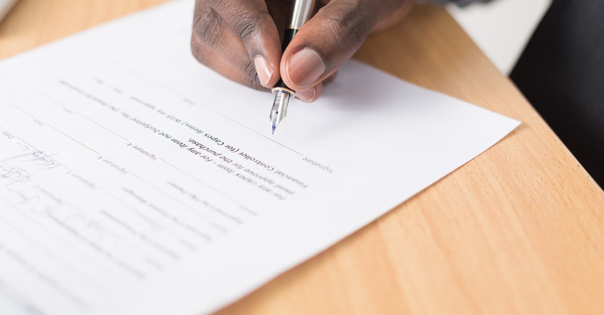 A hand holding a pen signing a document close-up on a desk, symbolizing agreement or contract finalization.