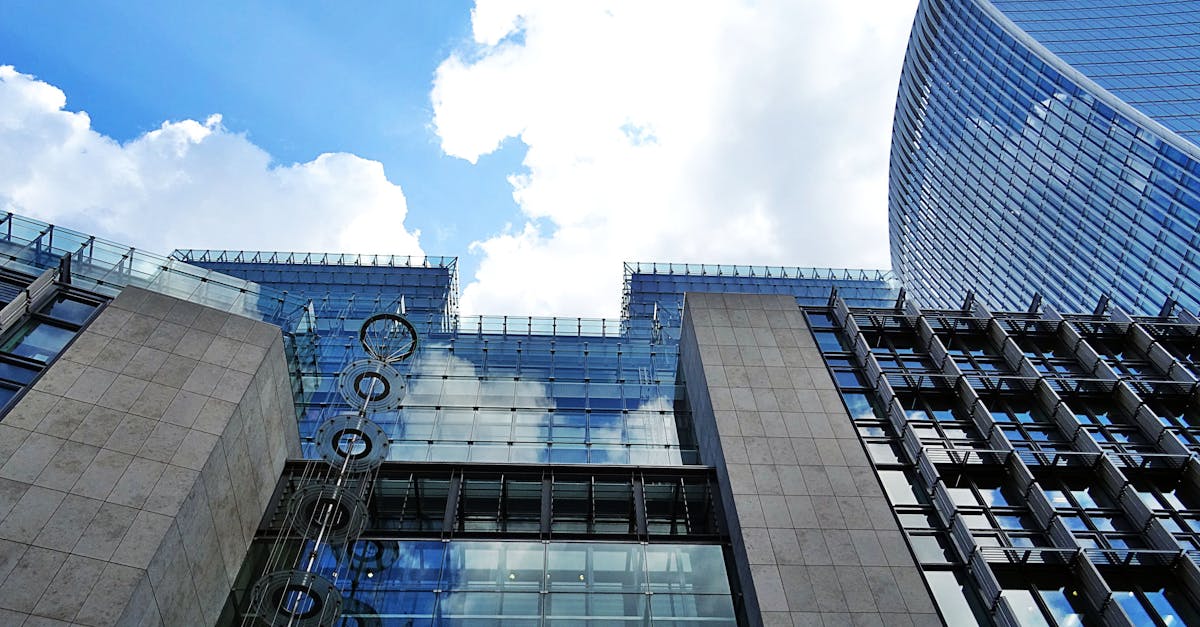 Futuristic glass and steel skyscraper with reflections against a bright blue sky.