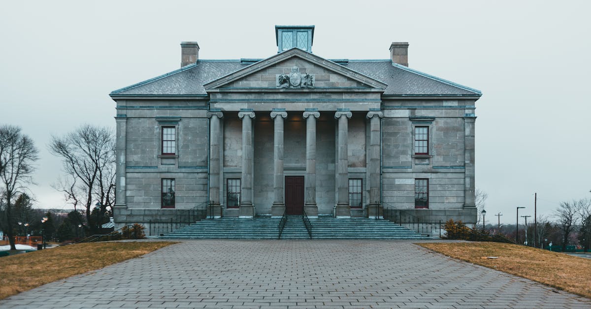 Exterior of aged stone building with columns and porch located near cobblestone pavement in gloomy weather