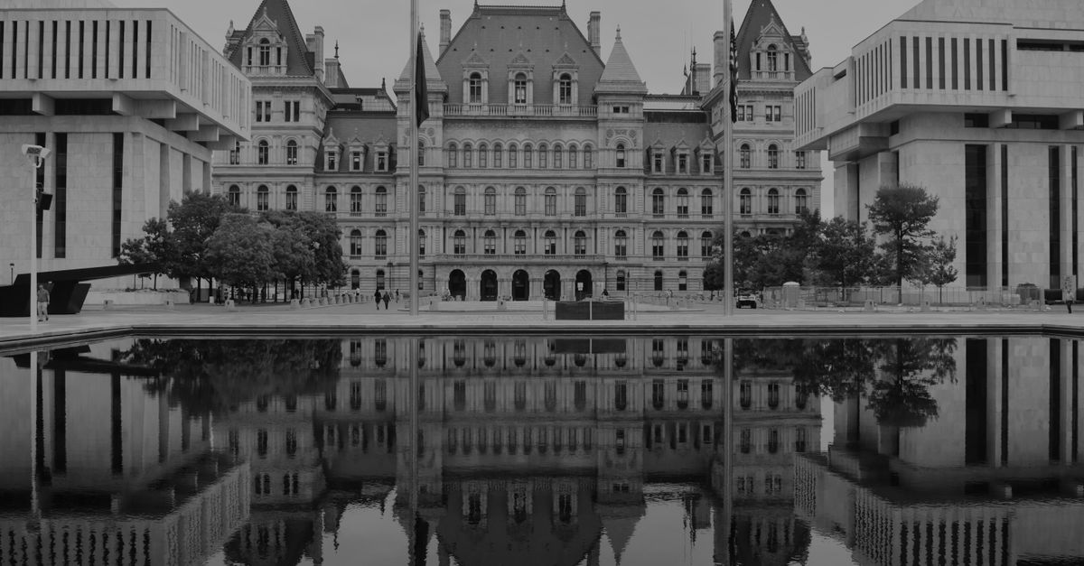 Monochrome photo of the New York State Capitol building with its reflection in water, emphasizing architectural symmetry.