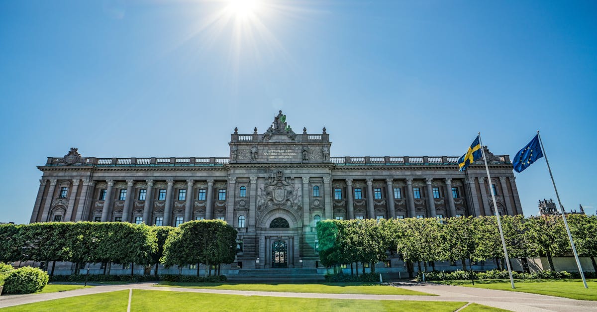 Front view of the Riksdag building with Swedish and EU flags on a sunny day.