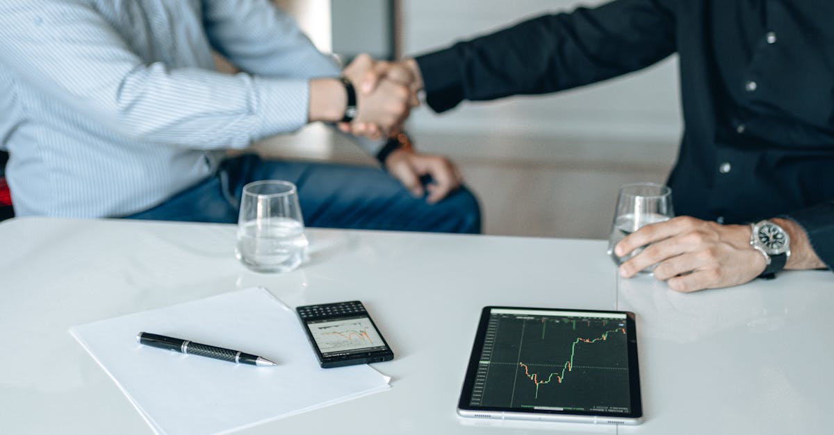 Business meeting with handshake and financial analysis displayed on a tablet.