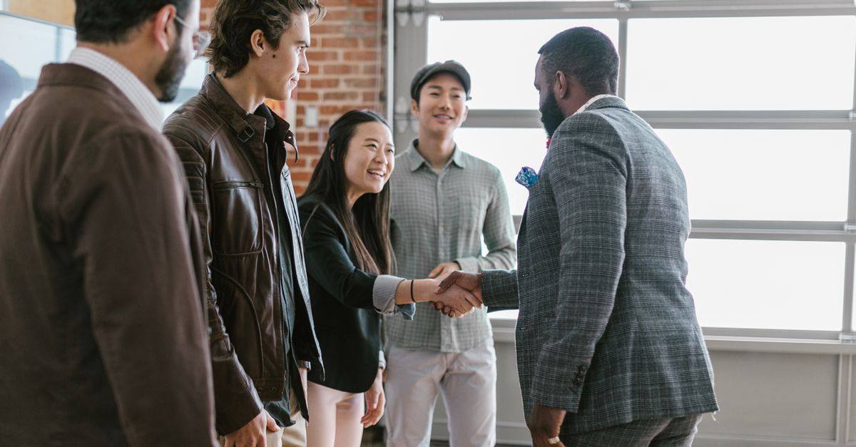 A diverse group of business professionals engaging in a handshake and discussion in a modern office space.