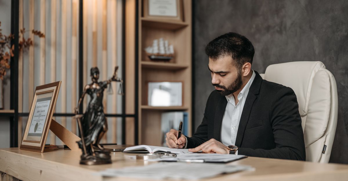A focused lawyer in an office setting writing and reviewing legal documents, symbolizing expertise and professionalism.