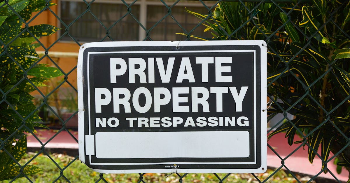 Close-up of a private property no trespassing sign on a chain-link fence with greenery in the background.