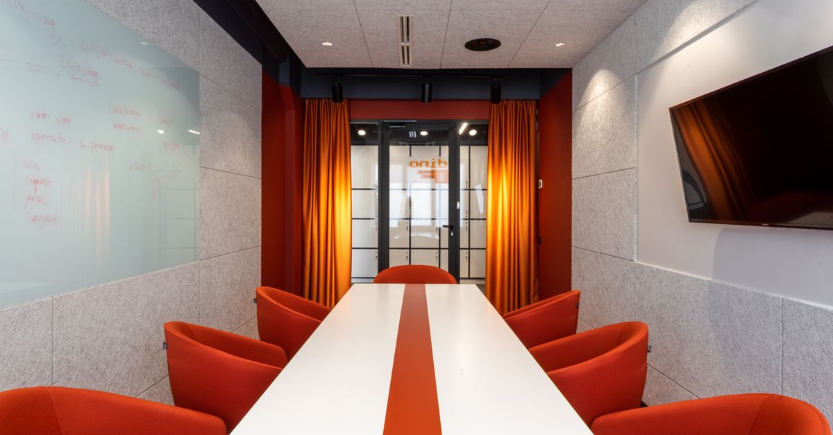 Set of comfortable orange armchairs placed around long white table in modern workspace with TV on wall and glass door