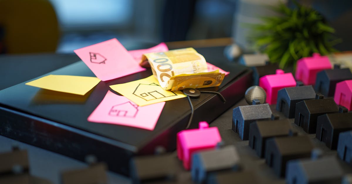 Euro banknotes on laptop with sticky notes and house models, symbolizing real estate investment.
