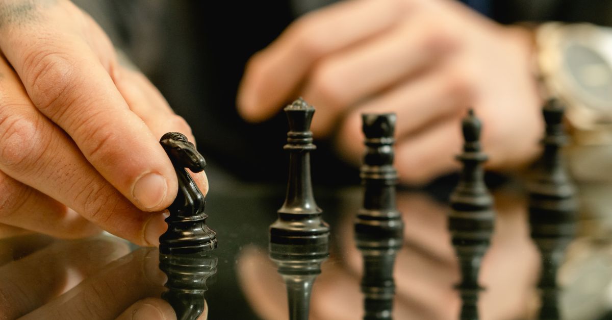 Close-up of a hand moving a chess piece on a reflective board, symbolizing strategy and decision-making.