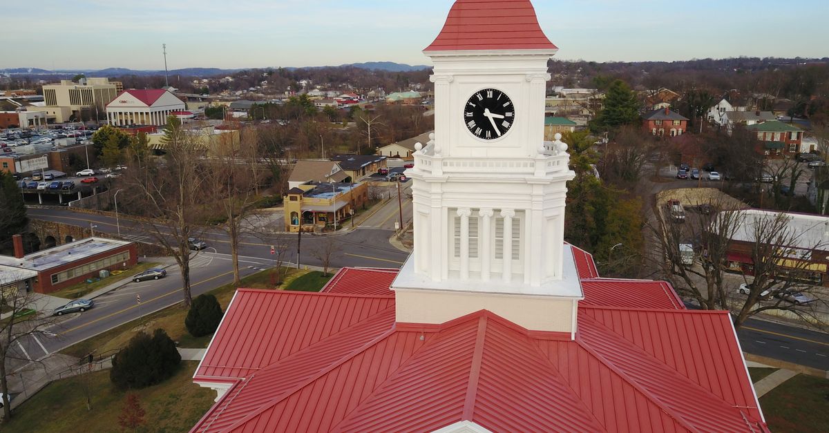 Aerial shot of a historic courthouse with clock tower featuring red roof and cityscape background.