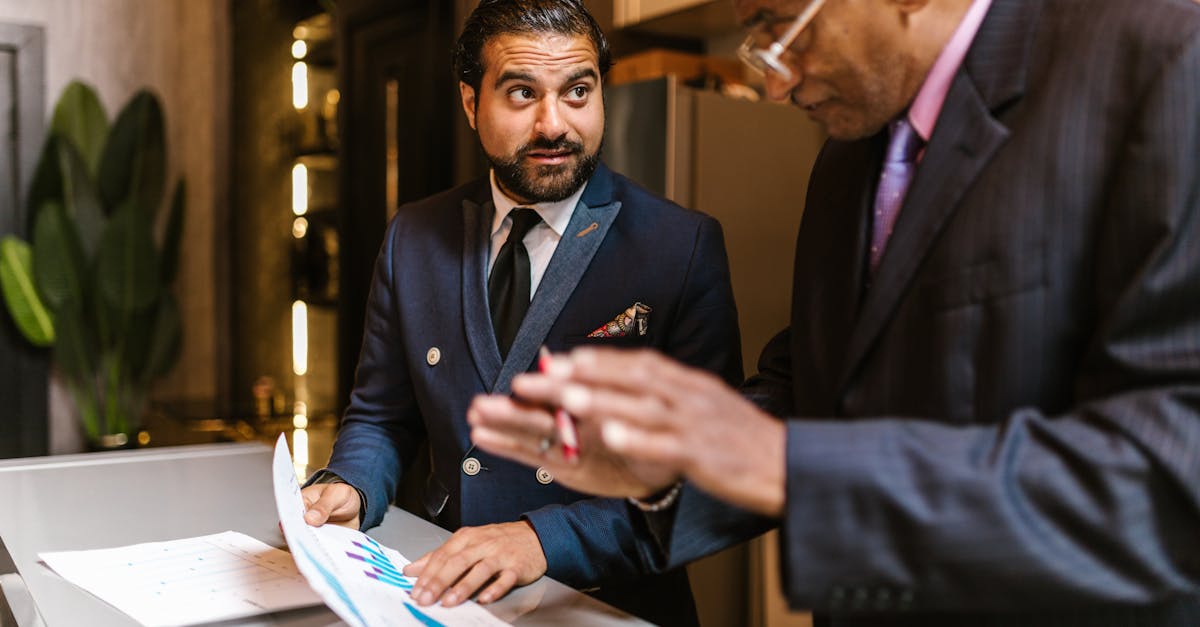 Two men in suits discuss financial documents with graphs indoors.