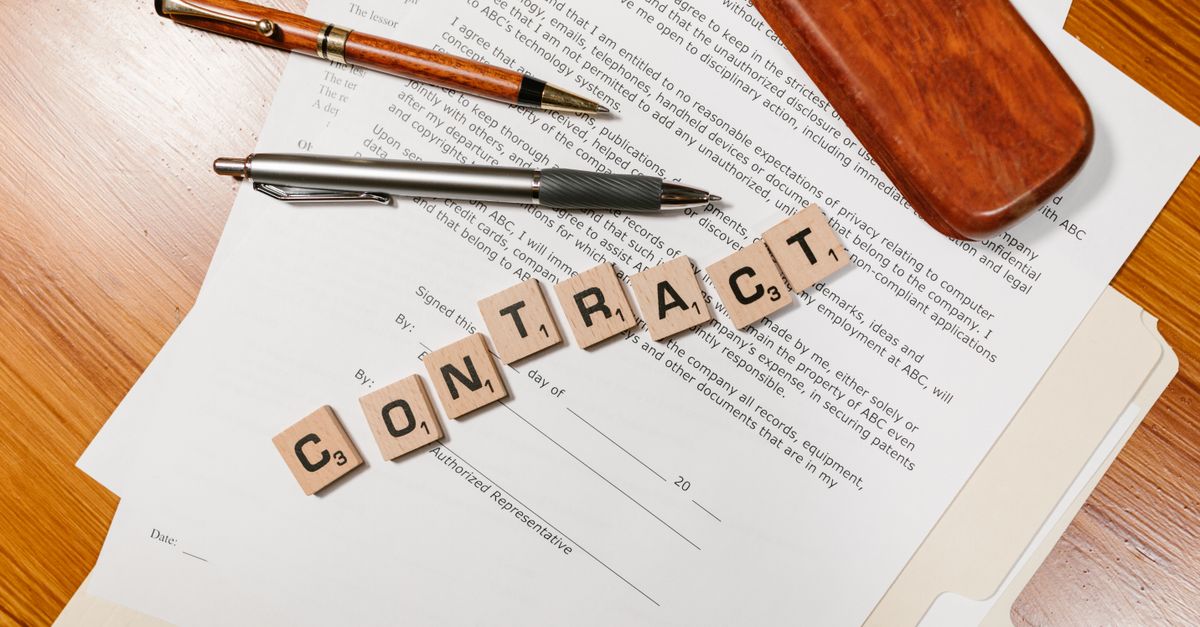 Close-up of contract papers with Scrabble tiles spelling 'CONTRACT'.