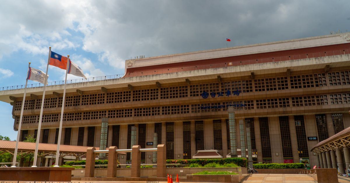 Taipei Main Station facade under cloudy sky with flags waving in Taiwan