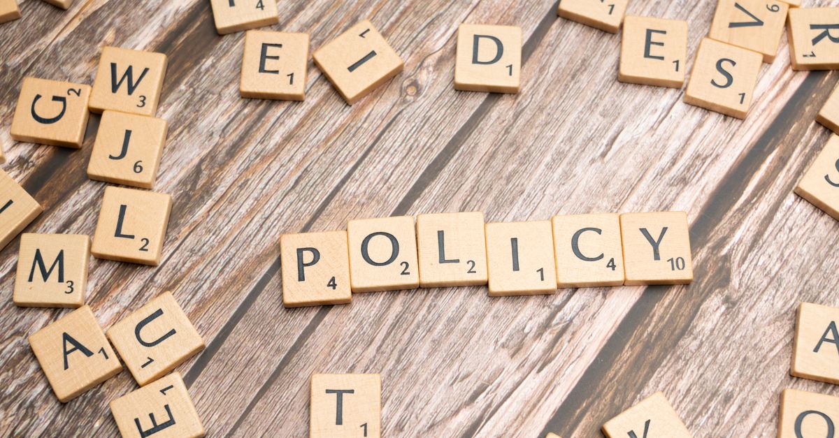 Scrabble letter tiles on a wooden background forming the word "Policy".