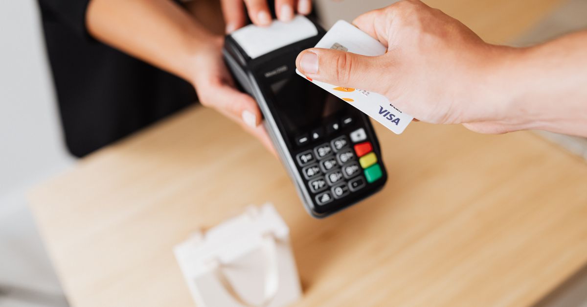 Close-up of hands using a contactless payment terminal with a credit card indoors.
