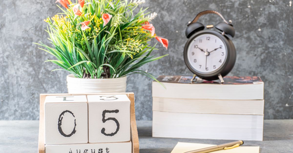 Stylish decorative arrangement featuring a calendar, clock, books, and a flower vase on a wooden surface.